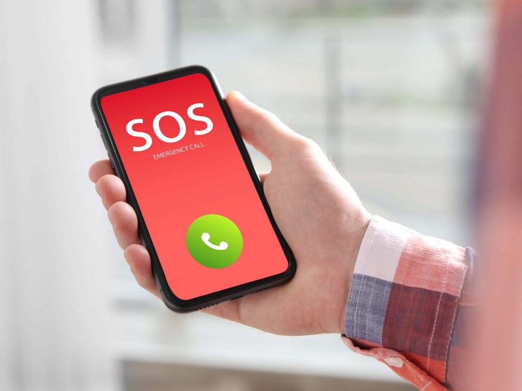 Hand hält Smartphone mit rotem Display, auf dem „SOS Emergency Call“ und eine grüne Anruftaste angezeigt sind